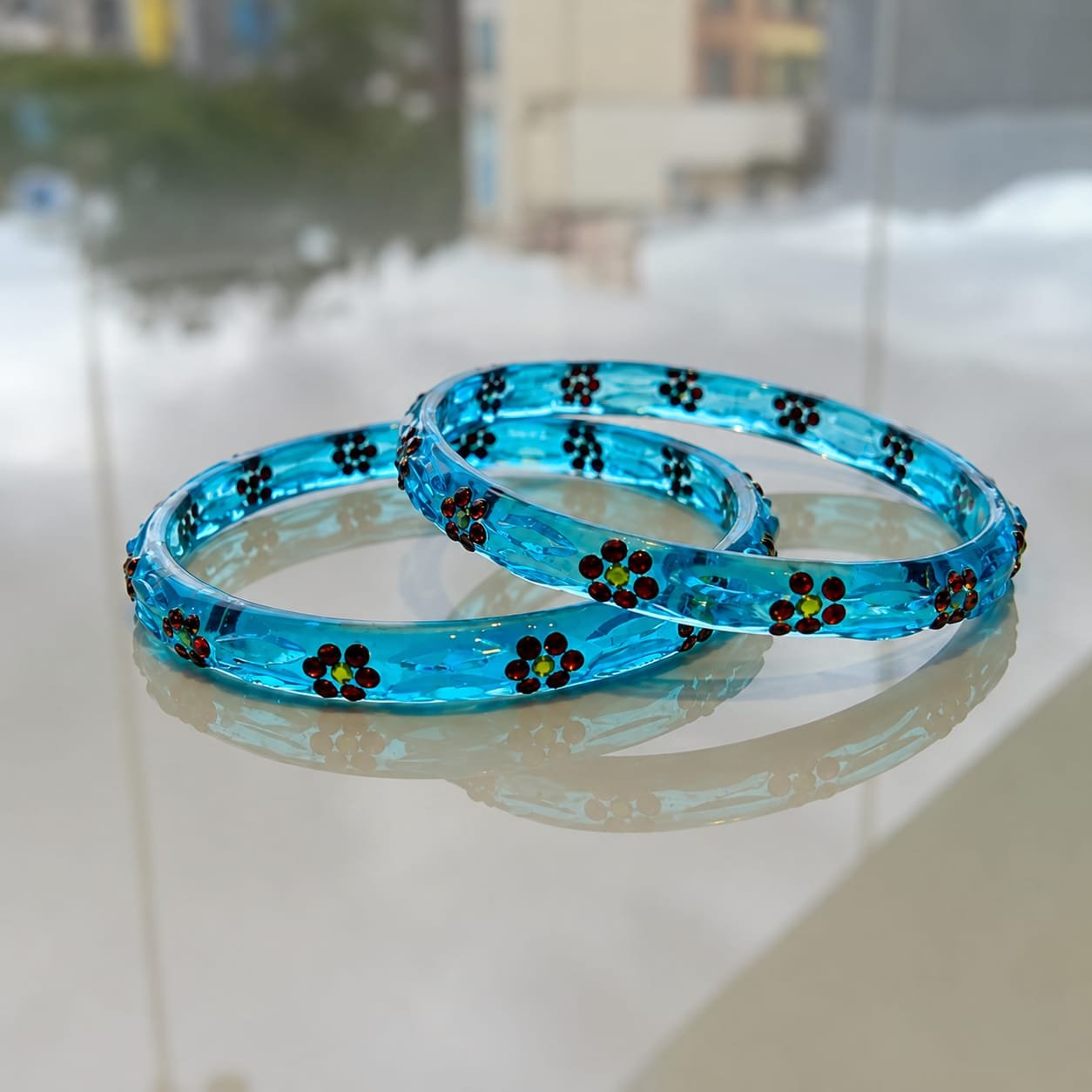 Sky blue crystal glass bangles decorated with tiny red and yellow floral rhinestone patterns.